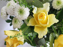 Kaunis kukkakimppu, jossa keltainen ruusu ja valkoiset krysanteemit, vihreillä lehdillä ja nupuilla koristeltuna.